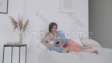 快乐的年轻母亲在她蹒跚学步的儿子睡觉前在数码平板电脑上展示卡通形象